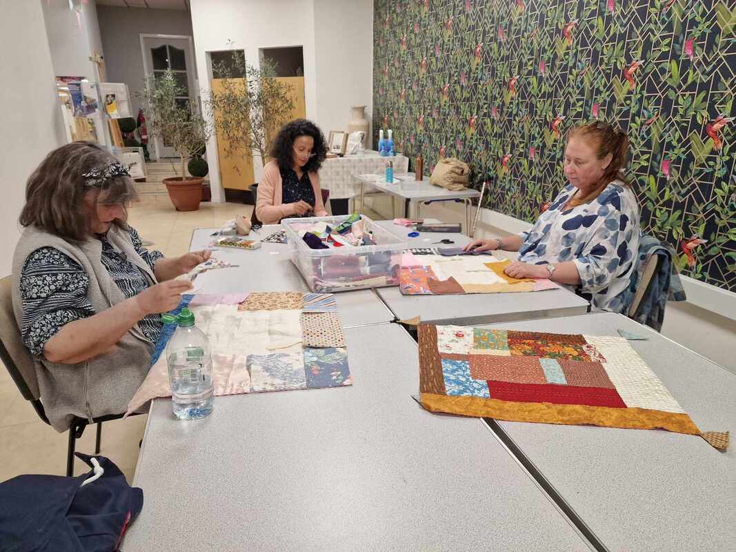 3 women sat at a table sewing fabric to make quilts in Midtown Makers workshop space
